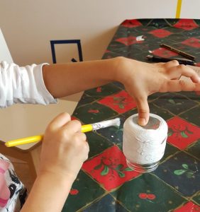 Kuvassa lapsi maalaa lasipurkkia valkoiseksi.