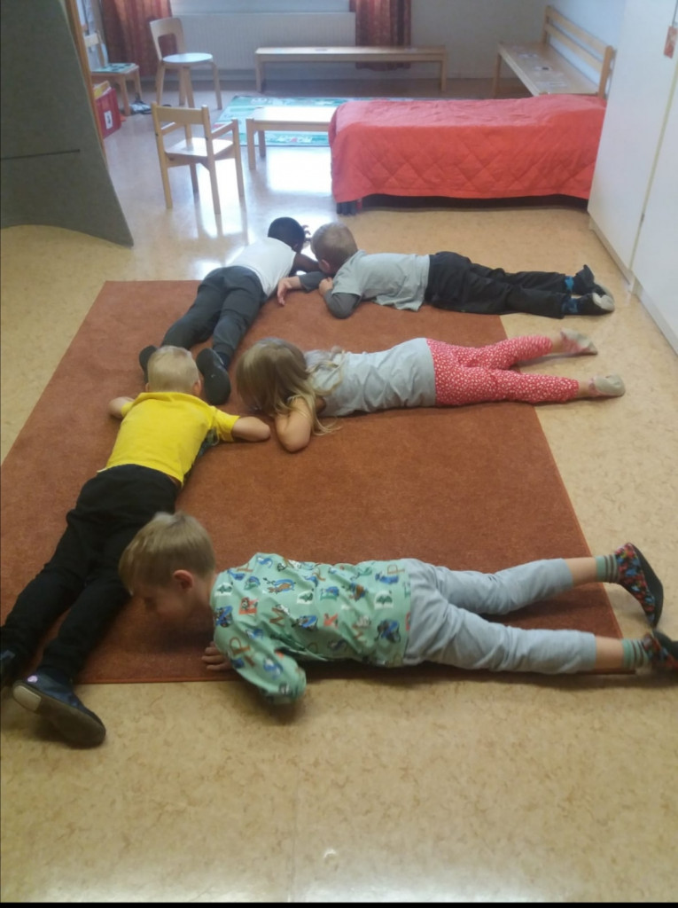 Lapset makaavat lattialla muodostaen kirjaimen E. 
