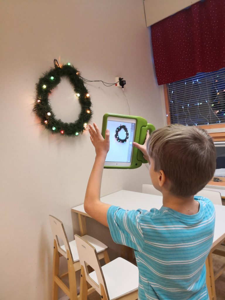 Lapsi ottaa kuvan ympyrän muotoisesta joulukoristeesta.