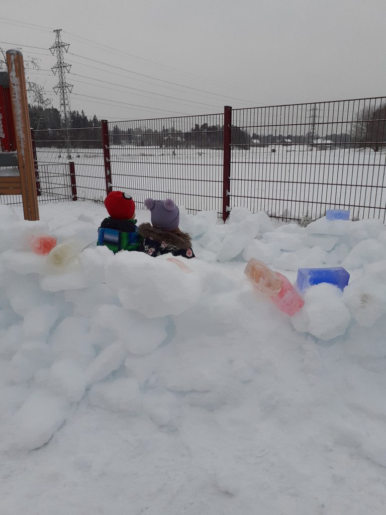 Kuvassa kaksi lasta lasten rakentamassa lumilinnassa.