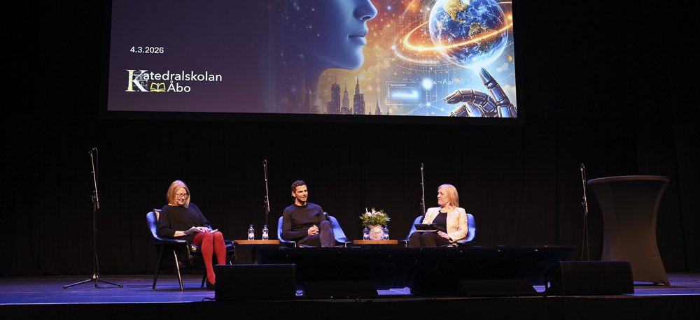 Tre personer sitter på en scen och diskuterar