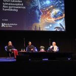 Tre personer sitter på en scen och diskuterar