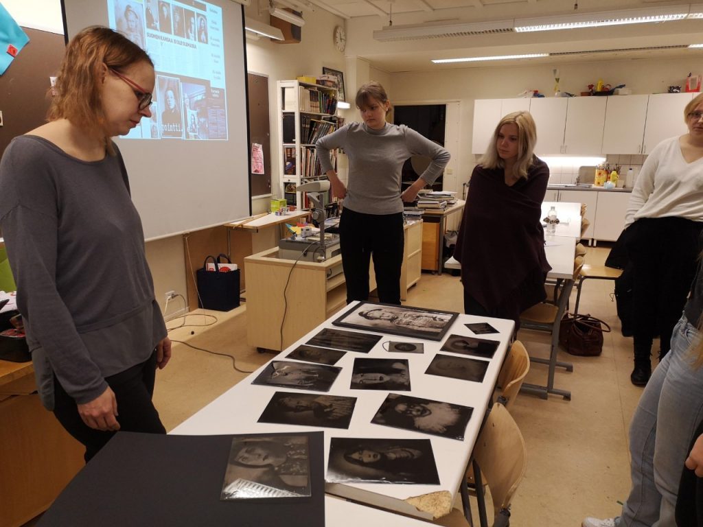 Joukko Porin lukiolaisia katsoo pöydällä olevia, alkuperäisellä valokuvaustekniikalla otettuja valokuvia, jotka on teetetty alumiinilevyille.