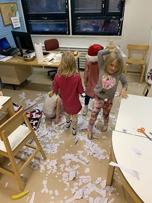 Neljä lasta leikkii lumella jonka he ovat tehneet paperisilpusta.