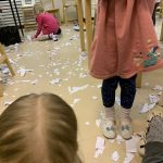 Kolme lasta kerää paperisilppua lattialta.