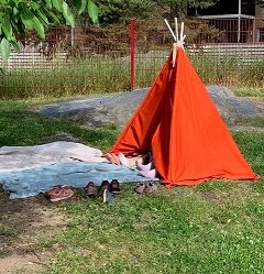 Tiipii-teltasta pilkistää lasten jalkoja. kengät ovat teltan ulkopuolella etualalla.
