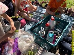 Viisi lasta istuvat viltillä ja heidän edessään on ostoskori jossa on juomapulloja. Lapset laittavat varrastikkuihinn viinirypäleitä ja vaahtokarkkeja.