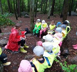 Lapset istuvat L-mallisesti puunrungoilla ja heidän edessään aikuinen esittelee heille sylissänsä olevaa pehmokettu.