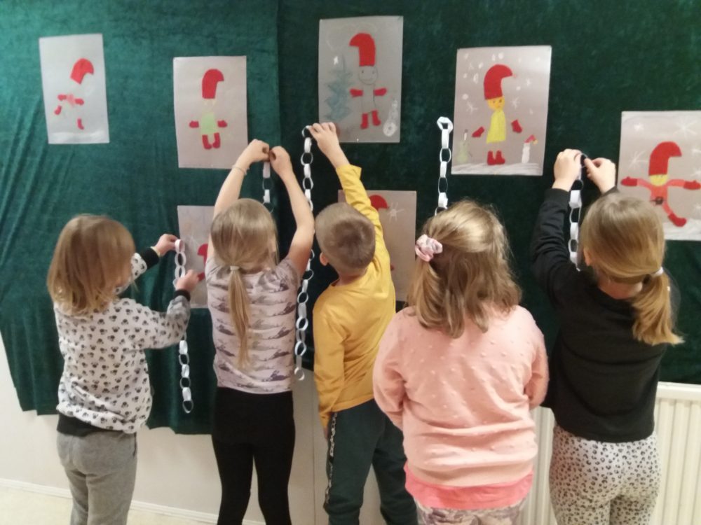 Lapset laittavat tekemiään joulukoristeita esille seinälle, tonttuaskartelut ja joulunauhaa