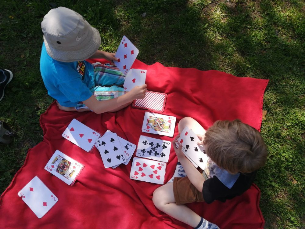 kaksi lasta pelaamassa korttia viltin päällä ulkona