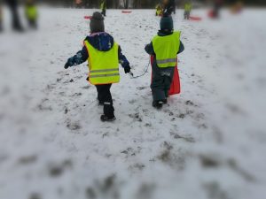 kaksi lasta kävelevät pulkkamäkeä ylospäin pulkka kädessä