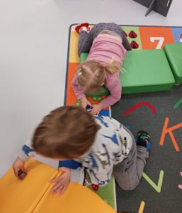 kaksi lasta leikkivät autoilla pehmopatjojen päällä