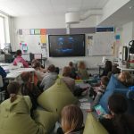 Oppilaat katsovat elokuvaa luokan lattialla.