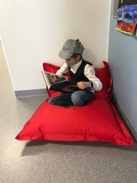 Sherlock Holmesiksi pukeutunut toisen luokan oppilas lukee kirjaa punaisessa säkkituolissa istuen.