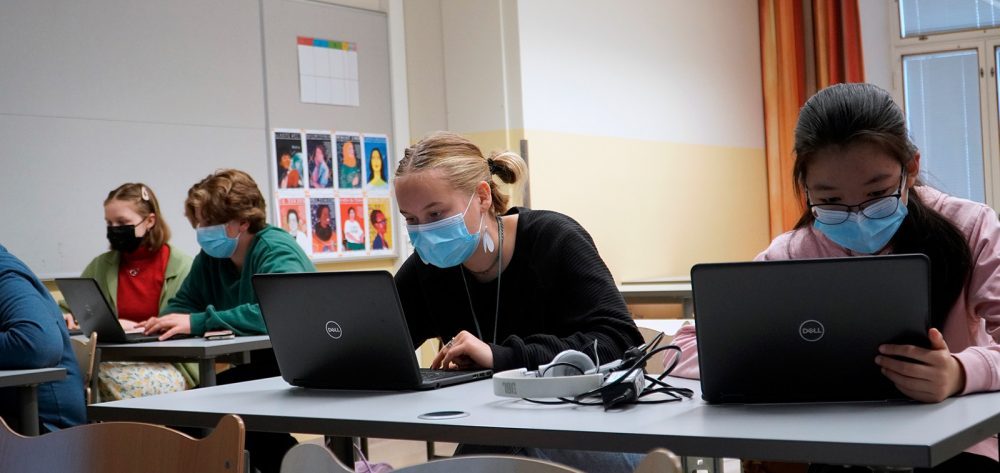Neljä oppilasta istuvat tarkkaavaisina tietokoneidensa ääressä. Heillä on maskit kasvoilla.