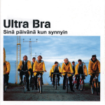 Yhdeksän Ultra Braan laulajaa pyöräilee keltaisissa sadetakeissa. Taustalla sinustä taivasta ja hiekkaista maata.