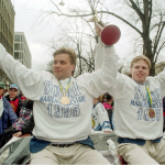 Kaksi jääkiekkoilijaa istuu auton katolla. Molemmilla on Suomen mestari 1995 -logolla varustetut valkoiset pelipaidat ja mitalit kaulassa.