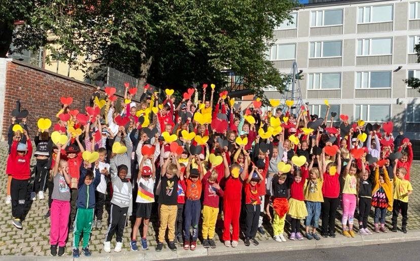 Saksanluokkien oppilaat ryhmäkuvassa koulun edessä Saksan lipun väreihin pukeutuneena