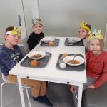 Neljä oppilasta syövät kouluruokailussa pahviset värikkäät kruunut päässään.