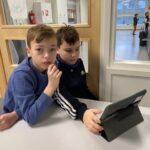 Kaksi poikaa pöydän kulmaan nojaten katselee iPadin ruutua.