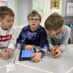 Kolme poikaa tutkii keskimmäisellä olevaa iPadin näyttöä.