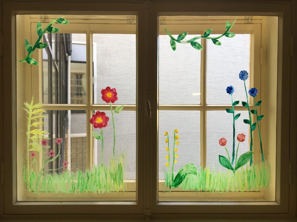 Ikkunamaalaus, jossa vesivärein on piirrettu ikkunaruutun kukkasia.