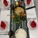 Kauniisti neljälle katettu ruokapöytä. Pöydällä nuudelirisottoa ja appelsiiniriisiä, sekä punaiset taitellut servietit valkoitilla lautasilla.