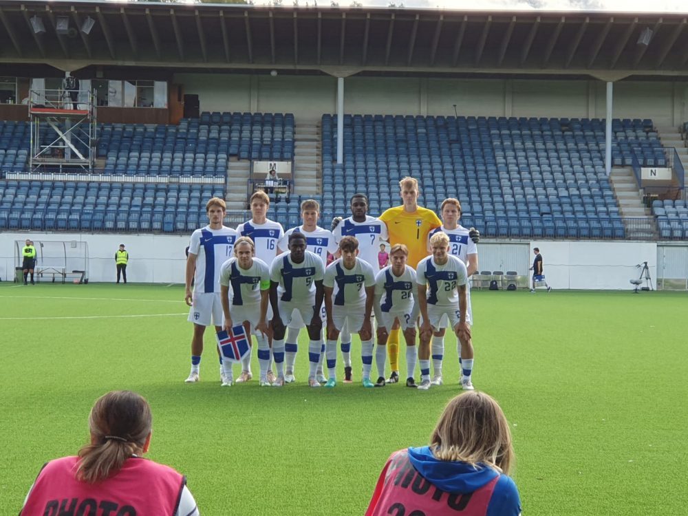 Viheriöllä kahdessa rivissä esiintyy Suomen nuorten jalkapallojoukkue. Taustalla nousee vielä tässä vaiheessa tyhjä katsomo.