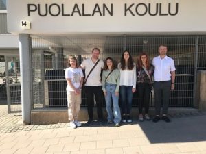 Kuvassa ulkona Puolalan koulun seinätekstin alla suomalaisia ja Espanjasta vierailevia opettajia.