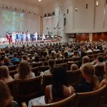 kuva otettu konserttisalin puolivälistä kohti lavaa. Yleisönä kuvassa koko yläkoulu. Lavalla kuoro.