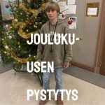 Poika seisoo koristellun joulukuusen edessä.