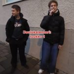 Kuvassa kaksi poikaa koulun seinän edessä. Toinen laittaa karkkia suuhunsa.