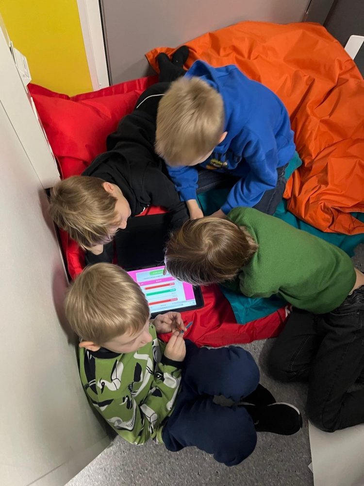 Neljä oppilasta pelaa Kielikarnevaali-peliä yhteisen ipadin äärellä.