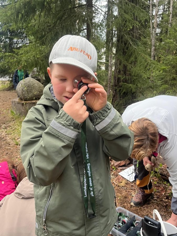 Oppilas tutkii luupilla hyönteistä metsäympäristössä.