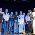 Oppilaita jotka esittävät robotteja lavalla. Etuoikealla ohjaajaoppilas painaa isosta näyttötaulusta komentokäskyjä roboteille.