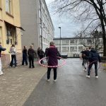 Opettaja ja oppilaita pyörittämässä hulavanteita koulun pihalla.