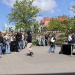 Oppilaita kesäisellä asfalttipihalla. Taustalla vehreä poisto ja sininen taivas.