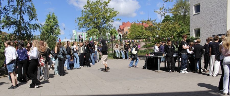 Oppilaita kesäisellä asfalttipihalla. Taustalla vehreä poisto ja sininen taivas.