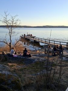 Nuoria rannalla. Osa istuu rantakallioilla, osa laiturin päässä.