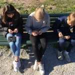 Kolme oppilasta istuu puistonpenkillä ja kirjoo pientä mustaa tilkkua, kukin omaansa.
