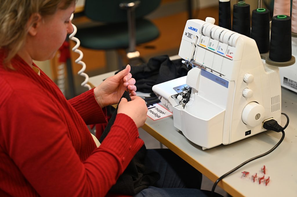 Kuvituskuva. Punapaitainen kurssilainen saumurin ääressä, työn touhussa.